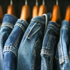 A row of denim jackets and jeans hanging on wooden hangers, showcasing different shades of blue denim, perfect for finding the best inexpensive jeans.