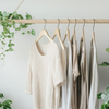 A minimalist wooden clothing rack with neutral-toned earth-friendly apparel, surrounded by lush green plants, creating a serene and sustainable fashion aesthetic.