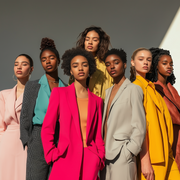 A strikingly diverse group of models, representing various ethnicities and cultural backgrounds, wearing Kokotete’s signature outfits. Each model is styled to showcase their individuality, with looks ranging from sleek tailored blazers and chic power suits to flowing dresses and modern separates. Set in a bright, sunlit studio, the models exude confidence and empowerment, standing together as a testament to Kokotete’s commitment to inclusivity and celebrating beauty in all forms. The clothing reflects the b