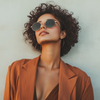 A stylish woman wearing a rust-colored sustainable blazer and round sunglasses, exuding confidence and effortless fashion against a neutral background, representing ethical and timeless style.