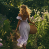 Model walking through a garden in a flowy lavender midi dress and straw bag - a classic summer colors clothes look inspired by the cool summer palette.